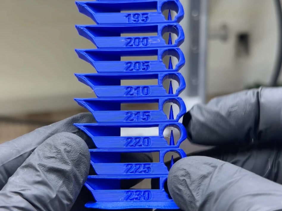 Torre de temperatura impressa em PLA Matte Azul Klein, de 195 a 230 °C, segurada com luvas na frente da impressora